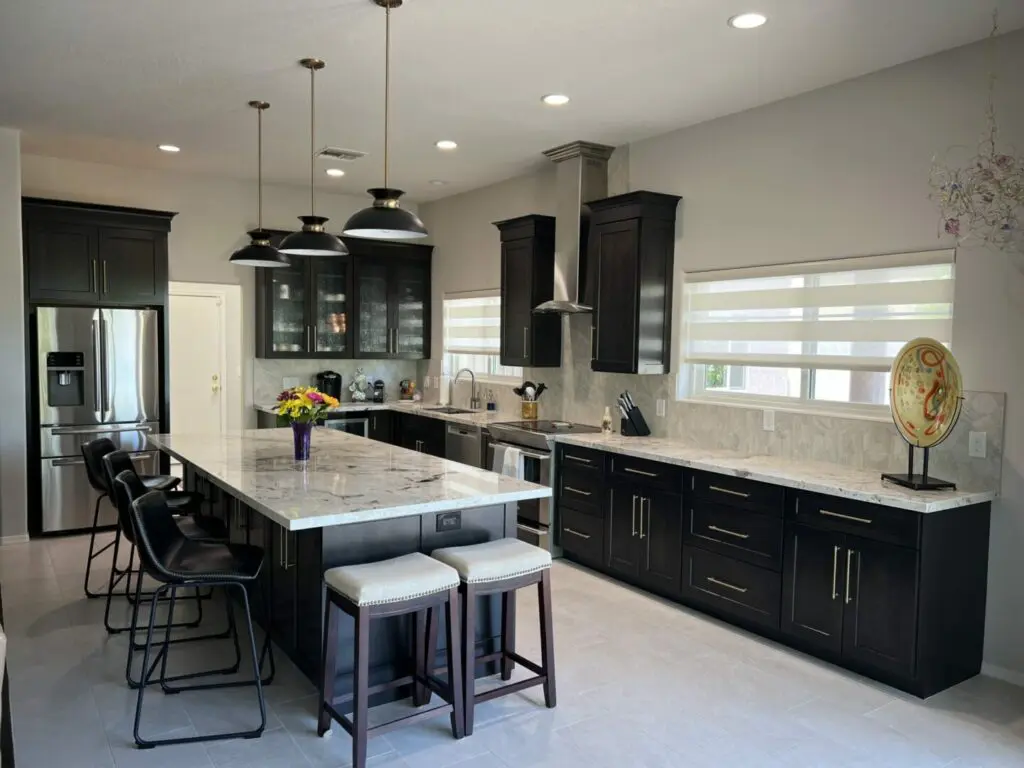 Modern kitchen with black cabinetry, marble countertops, stainless steel appliances, pendant lighting, and island seating for four