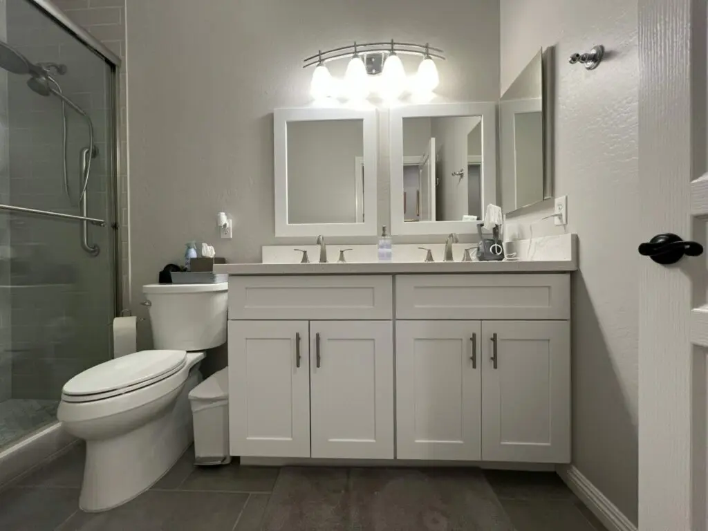 Modern bathroom with dual white vanity, two framed mirrors, chrome fixtures, and a walk-in shower with glass enclosure