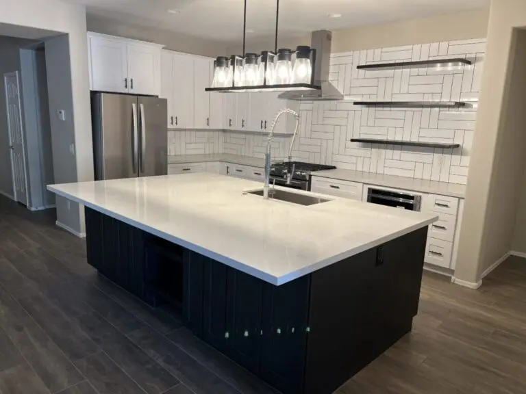 Modern kitchen with white cabinetry, black island with white countertop, stainless steel appliances, herringbone tile backsplash, and floating shelves