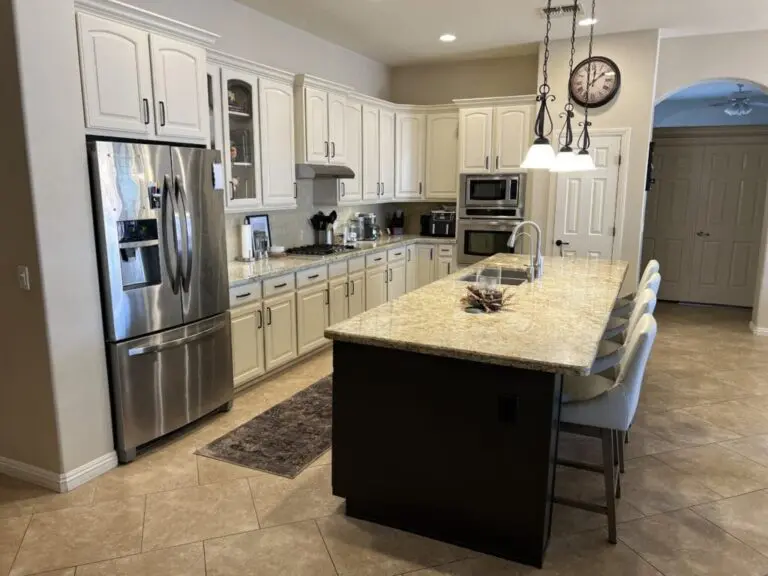 Modern kitchen with cream cabinets, black island with light countertop, stainless steel appliances, pendant lighting, and tile flooring