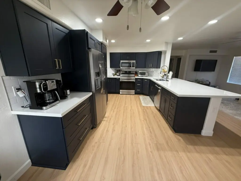 Modern kitchen with dark navy cabinetry, white quartz countertops, stainless steel appliances, white subway tile backsplash, and light wood-look flooring