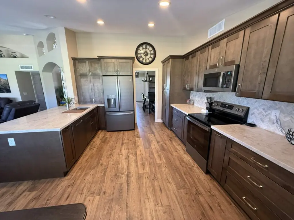 Modern kitchen with dark wood cabinetry, stainless steel appliances, quartz countertops, herringbone backsplash, and wood-look flooring