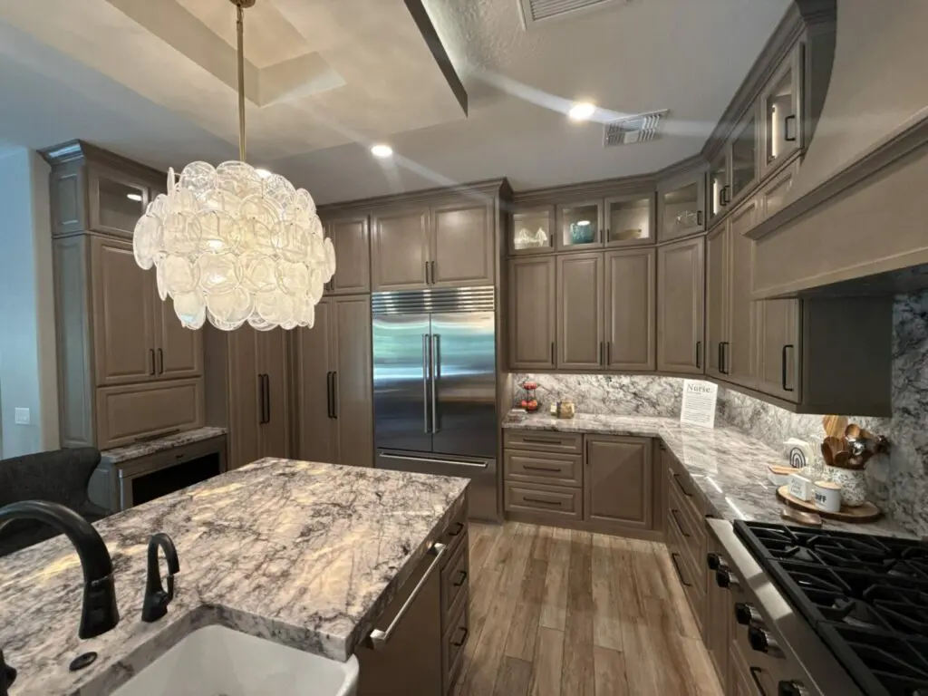 Modern luxury kitchen with gray cabinetry, marble countertops, stainless steel appliances, island seating, and a decorative pendant light fixture