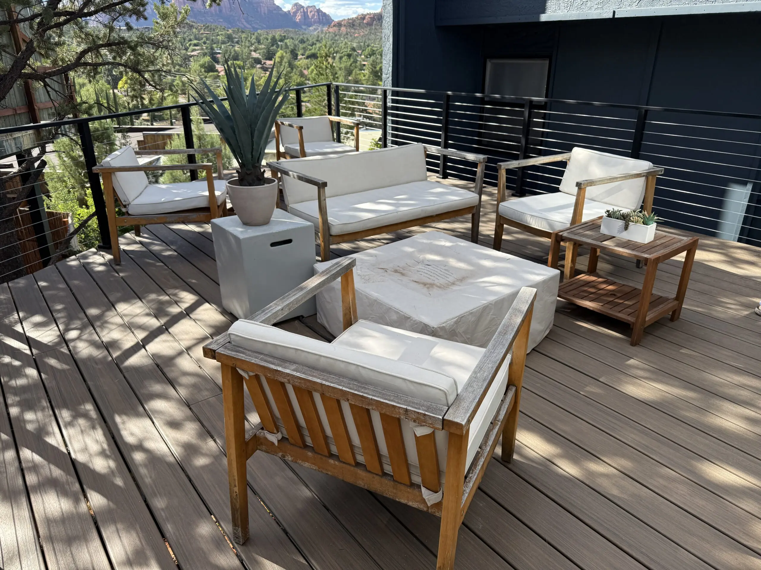Modern rooftop patio with wooden furniture, white cushions, fire pit, and mountain views in background