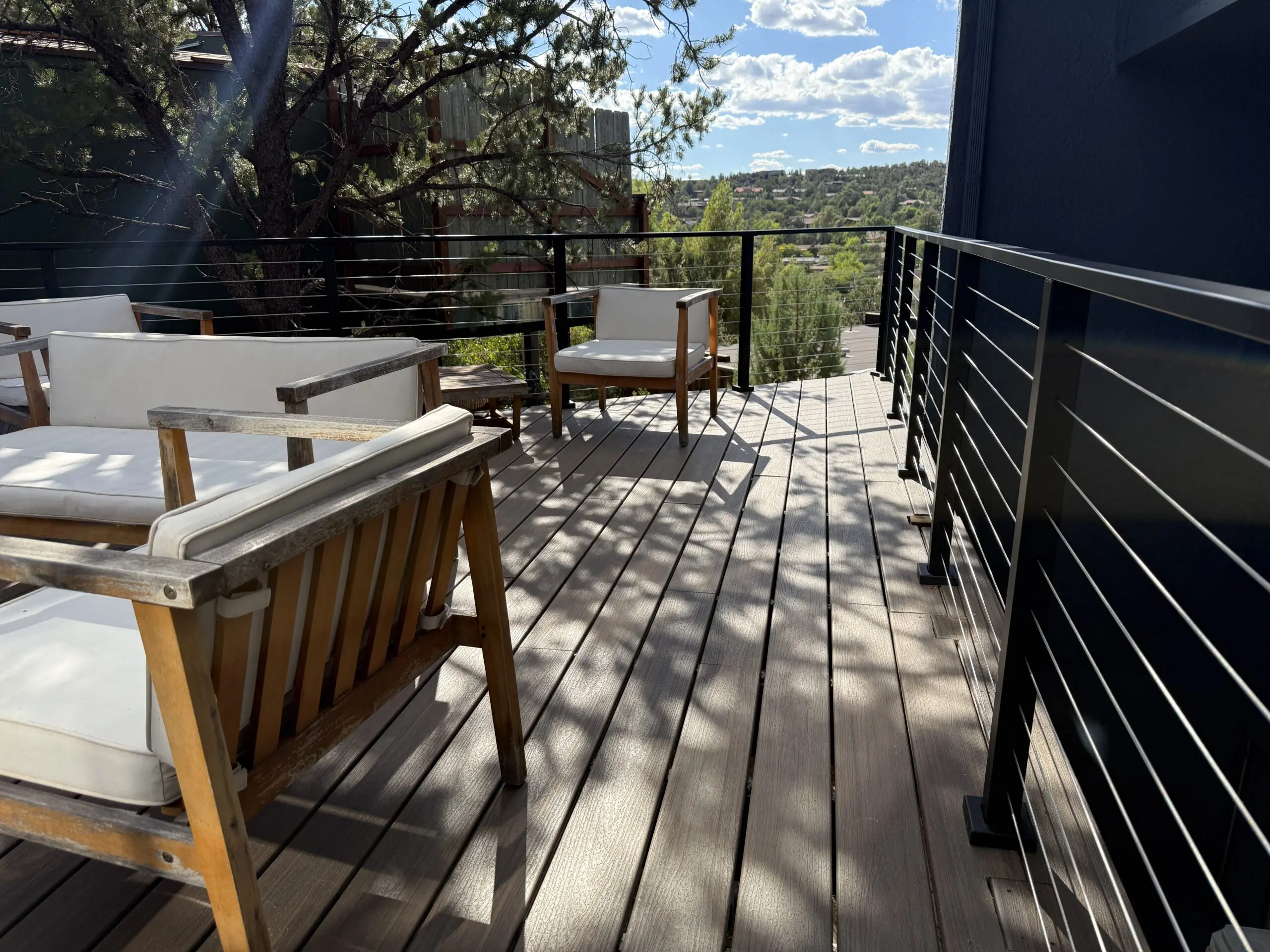 Modern hilltop deck with wooden lounge chairs, black metal railing, and expansive view of forested hillside landscape under blue sky