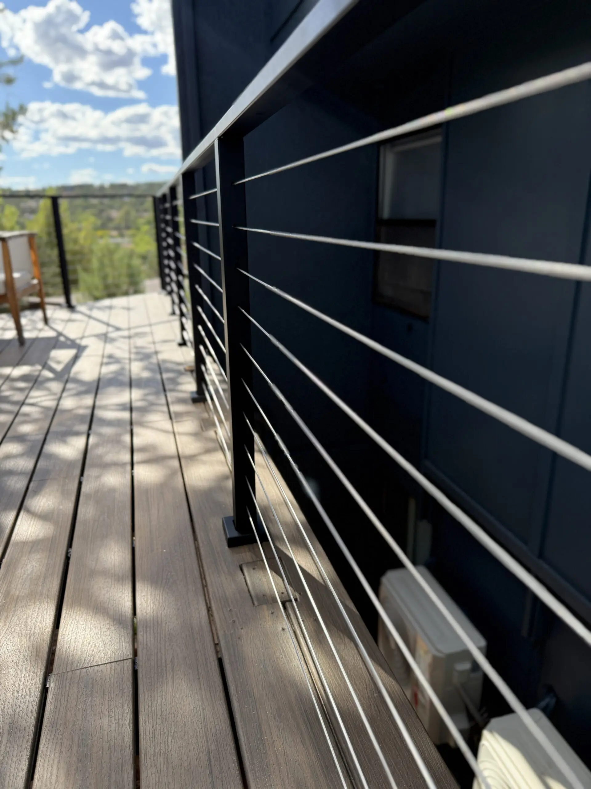 Modern deck with horizontal stainless steel railing overlooking green landscape under blue sky with white clouds