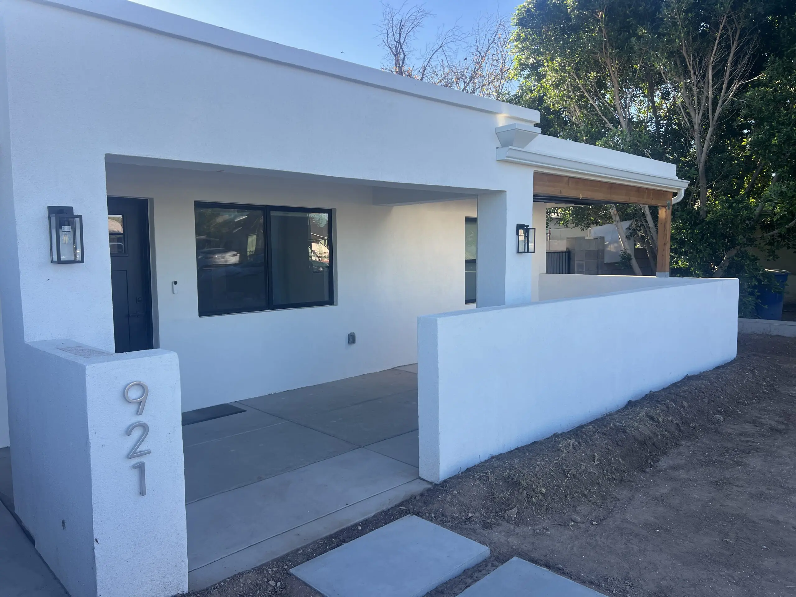 Modern white residential home with black-framed windows and doors, white fence, and wooden pergola, numbered 921 on street corner