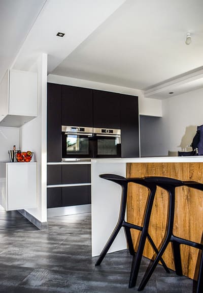 A kitchen with black and white cabinets, a bar stool, and an oven.