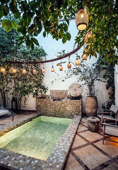 A pool surrounded by trees and chairs in an outdoor area.