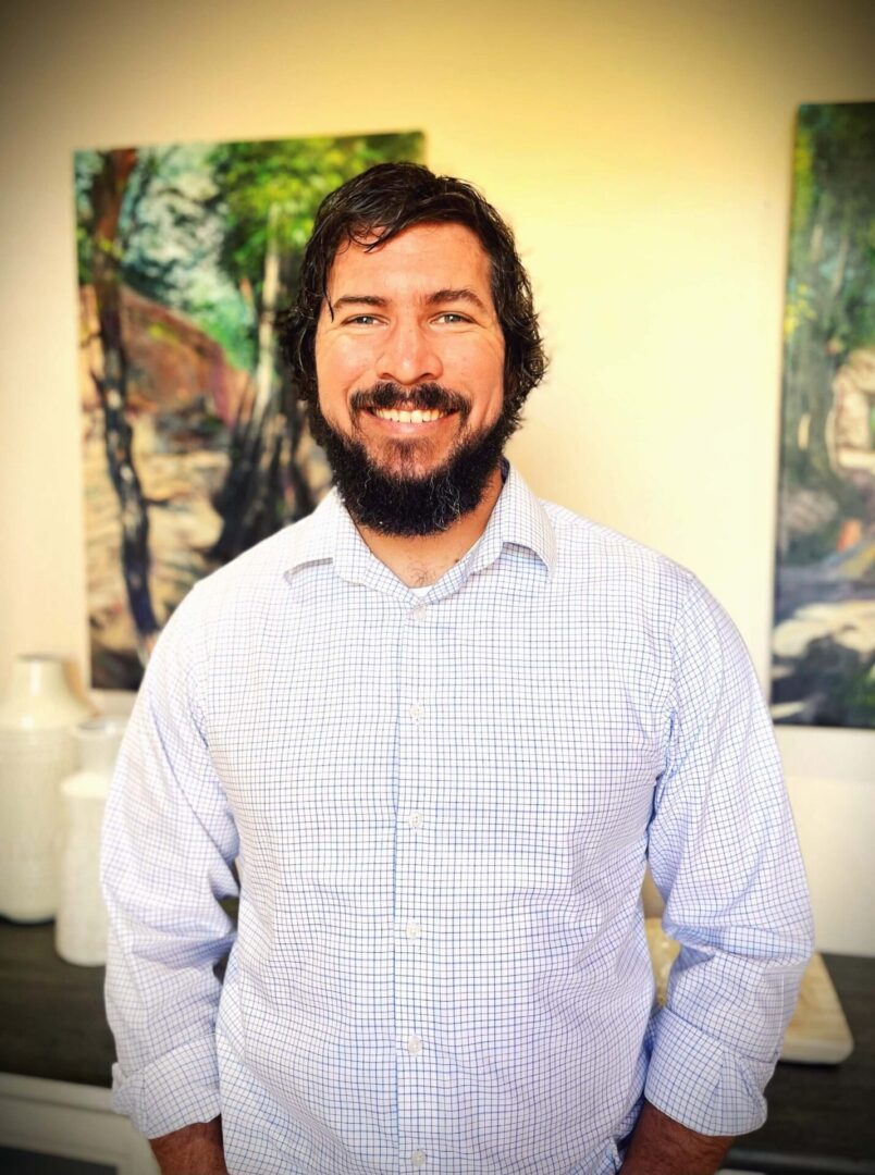 A man with long hair and beard standing in front of a painting.