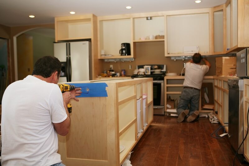 Two workers are busy installing new quality cabinetry in a kitchen. This image captures an essential phase in the kitchen remodeling process and highlights the importance of craftsmanship and high-grade components.