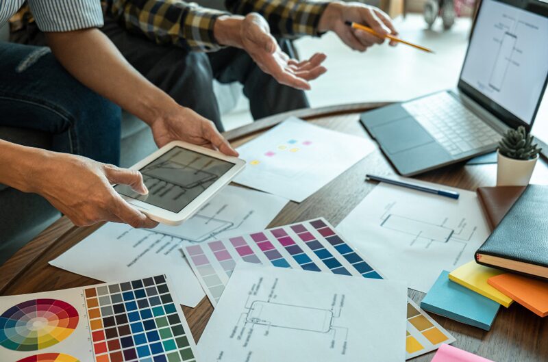 A group of people collaborate over design plans and color swatches, discussing ideas and options for a phoenix kitchen remodeling project. 