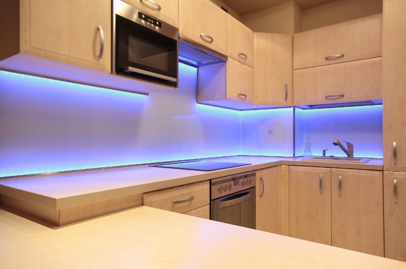 A modern kitchen features sleek cabinetry and vibrant blue LED under-cabinet lighting, showcasing the results of a kitchen and home renovation.