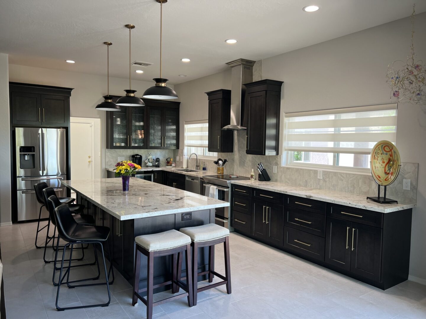 Modern kitchen with black cabinetry, marble countertops, stainless steel appliances, pendant lighting, and island seating for four
