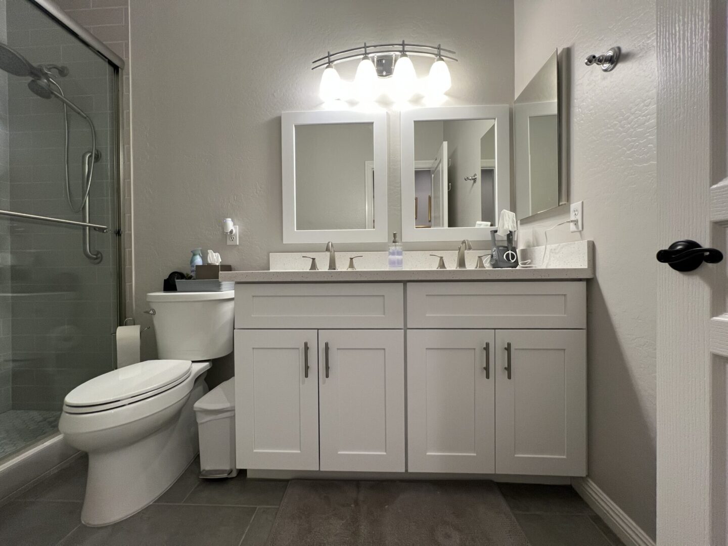 Modern bathroom with dual white vanity, two framed mirrors, chrome fixtures, and a walk-in shower with glass enclosure