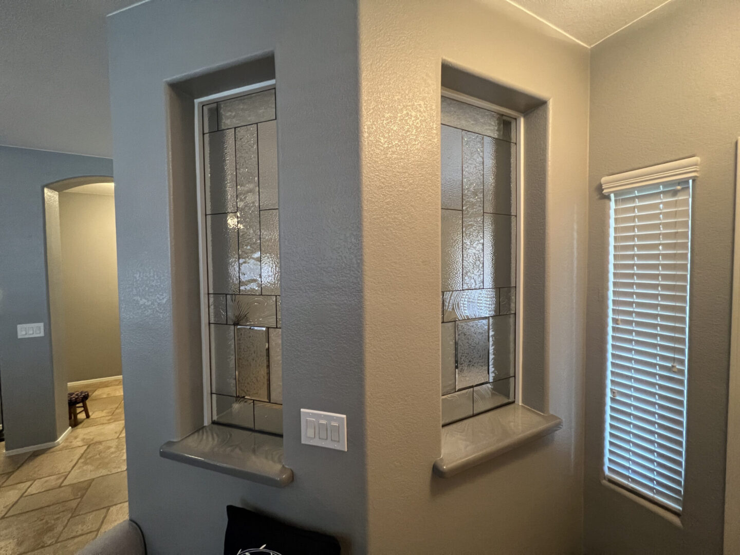 Modern bathroom with dual frosted glass windows with black frames, beige textured walls, white blinds on right window, and neutral tile flooring