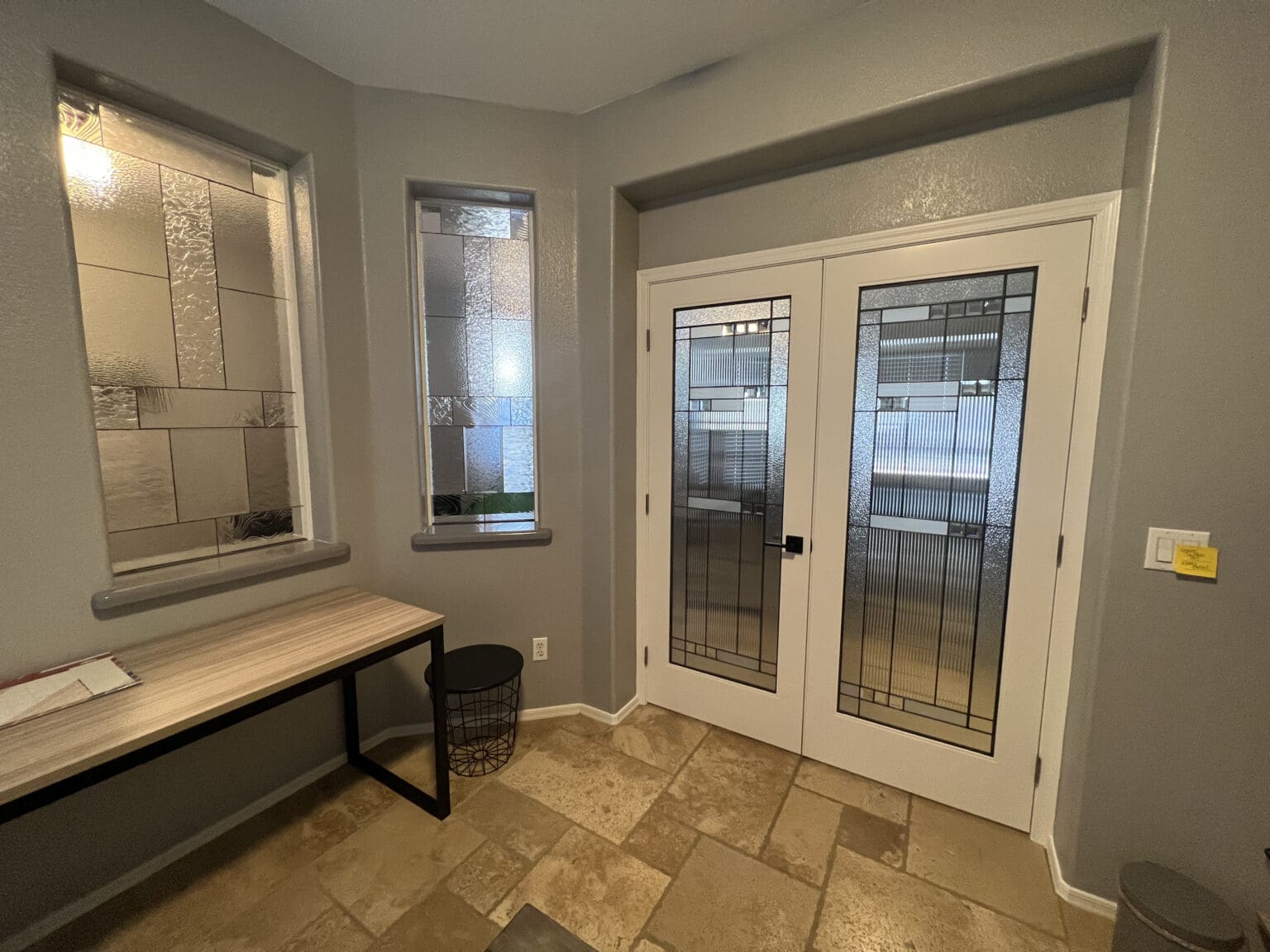 Modern bathroom showroom with glass-enclosed shower, dual French doors with decorative glass panels, floating wooden vanity, tile flooring, and display windows showcasing bathroom fixtures and design options