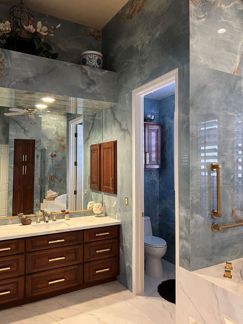 Luxury master bathroom with dark veined marble walls, dark wood vanity with brass hardware, large mirror, walk-in shower with glass enclosure, and separate toilet room