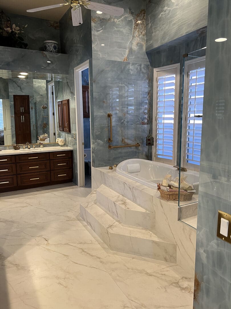 Luxury master bathroom with marble flooring and walls, featuring a freestanding soaking tub with glass shower enclosure, dark wood vanity, and shuttered windows