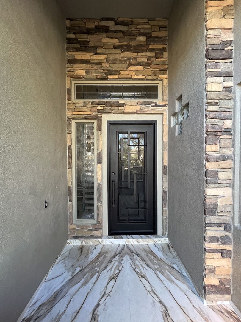 Modern entryway with black front door, marble flooring, stone accent wall, and sidelights leading to residential home