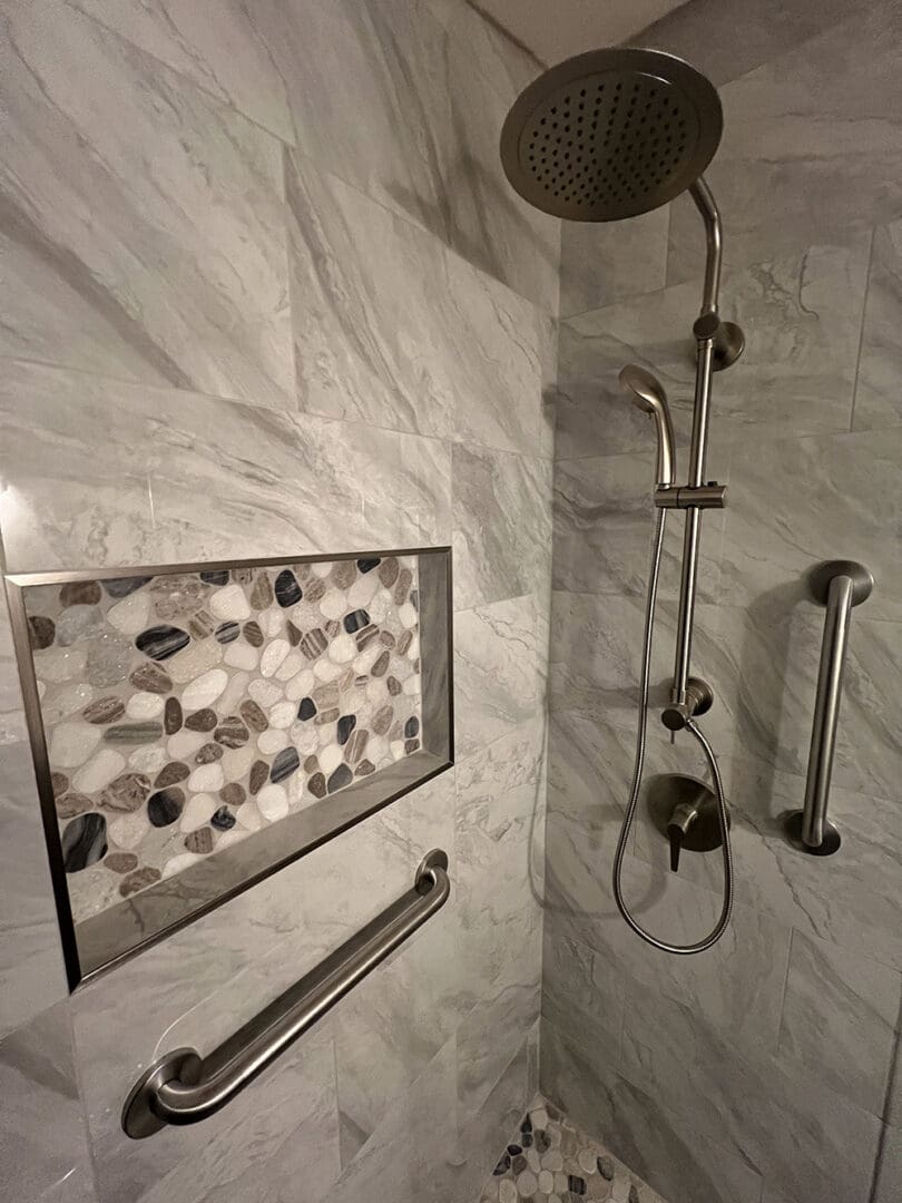 Modern bathroom shower with marble tile walls, rainfall showerhead, handheld spray, brushed nickel fixtures, and decorative pebble tile niche