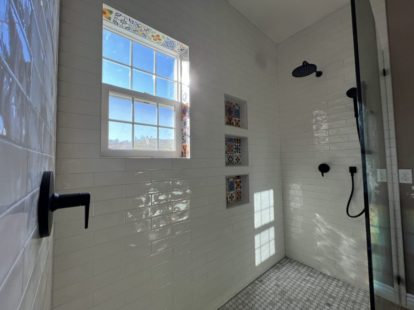 Modern walk-in shower with white subway tiles, black fixtures, rainfall showerhead, decorative ceramic tiles, large window with city skyline view, and glass enclosure
