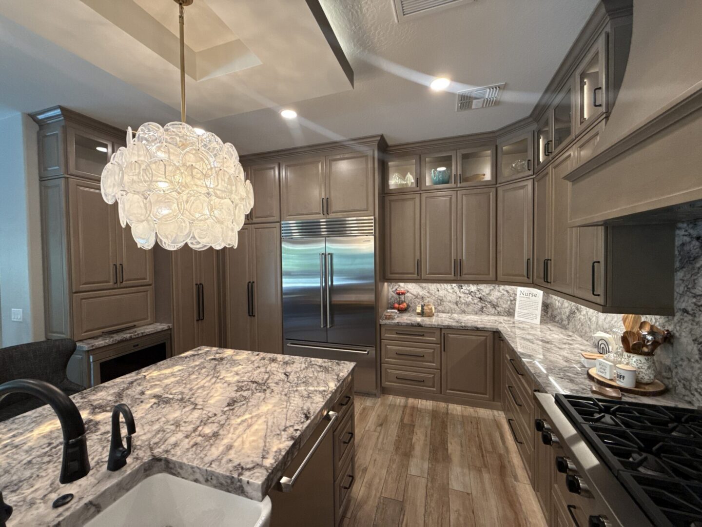 Modern luxury kitchen with gray cabinetry, marble countertops, stainless steel appliances, island seating, and a decorative pendant light fixture