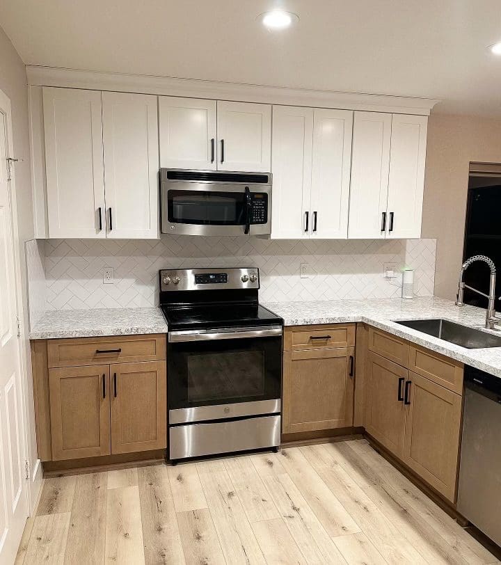 Modern kitchen with white upper cabinets and natural wood lower cabinets, stainless steel appliances, granite countertops, herringbone backsplash, and light wood flooring