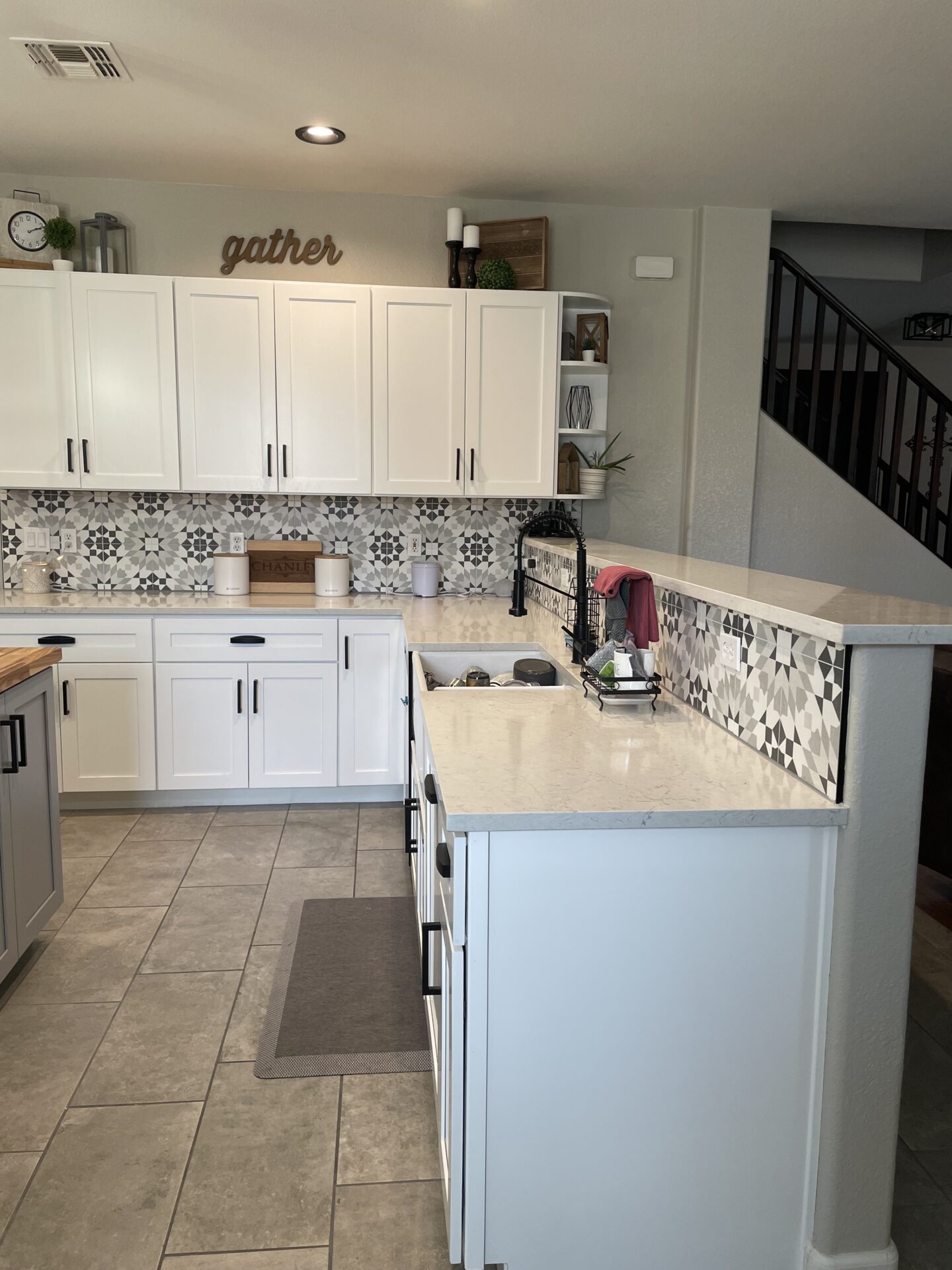 Modern kitchen with white cabinetry, marble countertops, and geometric black and white tile backsplash, featuring an island with bar seating and open shelving above