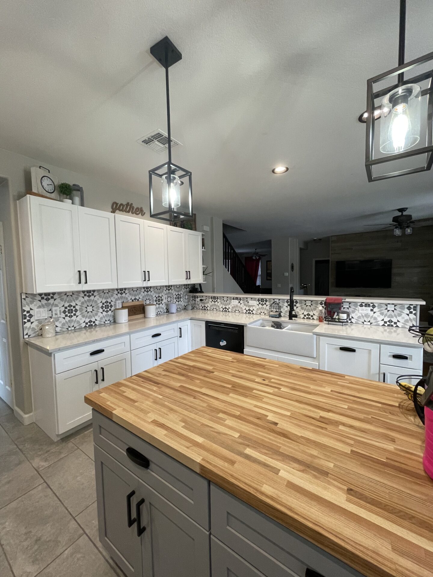 Modern kitchen with white cabinetry, patterned backsplash, butcher block island, farmhouse sink, and black pendant lighting fixtures