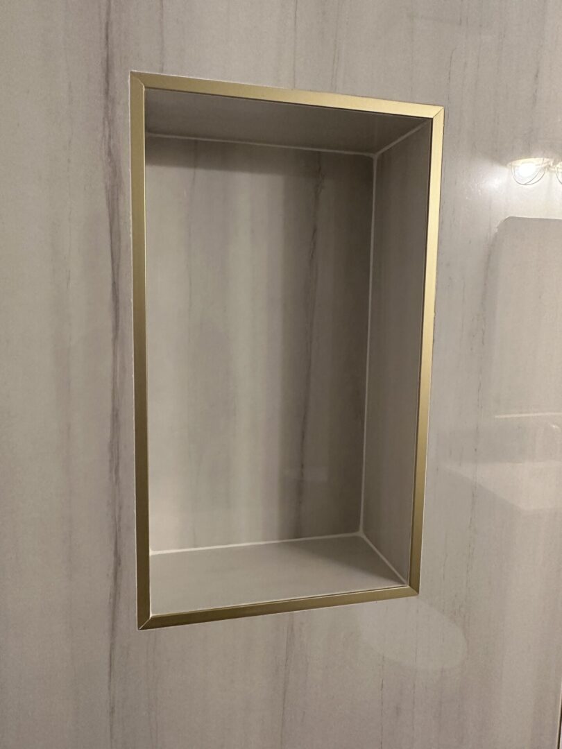 Empty recessed wall niche with gold trim and white interior shelving in modern bathroom or shower area