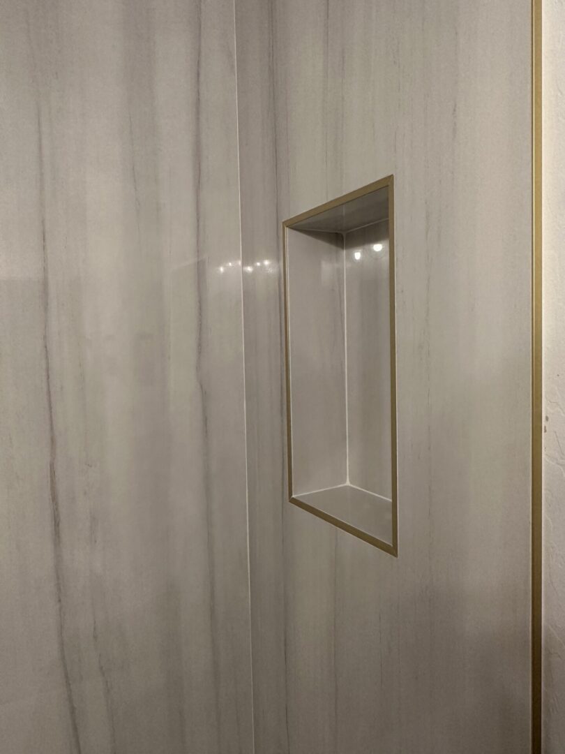 Empty glass display case with brass frame mounted on light marble wall with recessed lighting inside the case