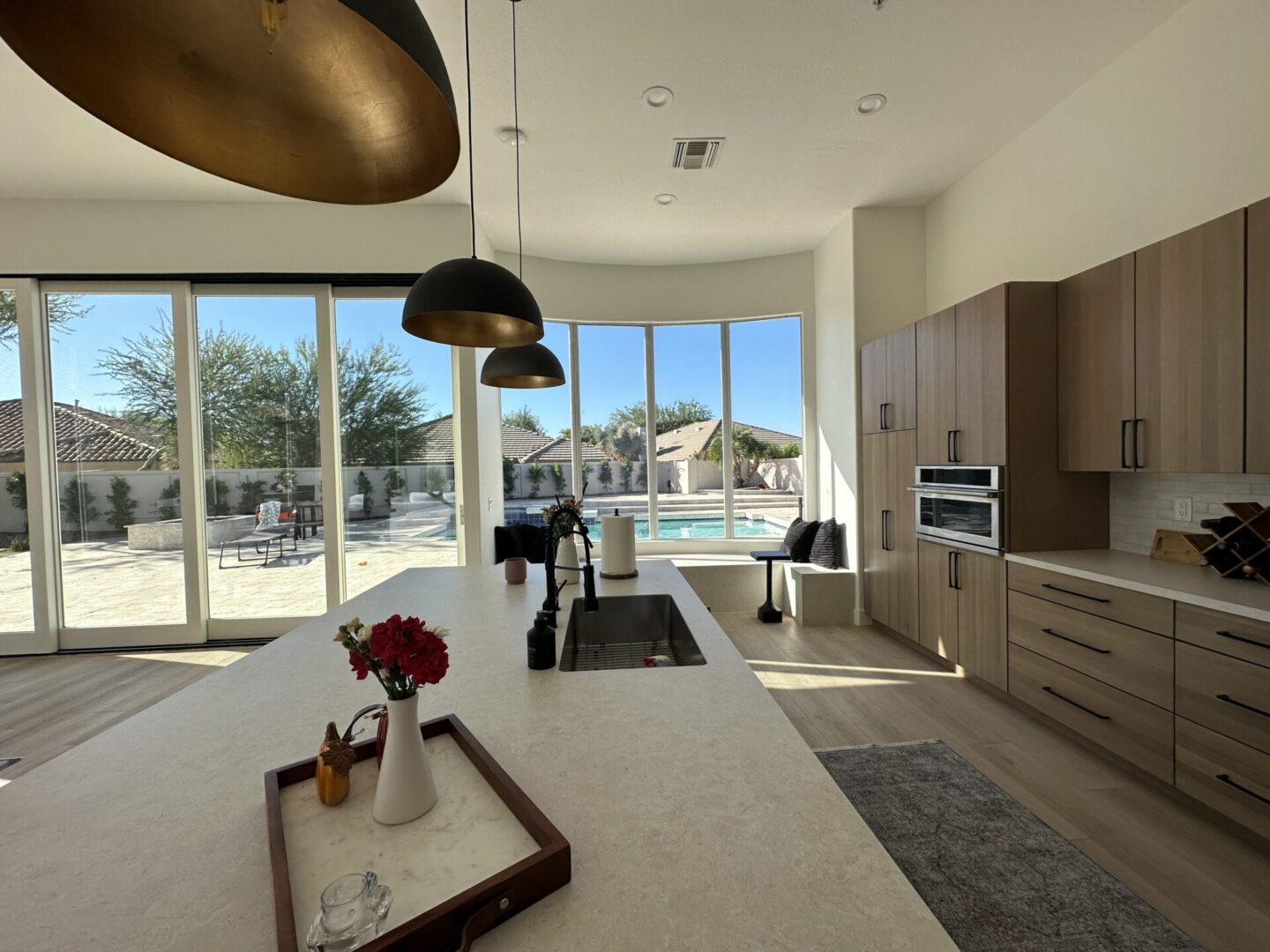 Modern luxury kitchen with island, pendant lights, and floor-to-ceiling windows overlooking backyard pool and patio