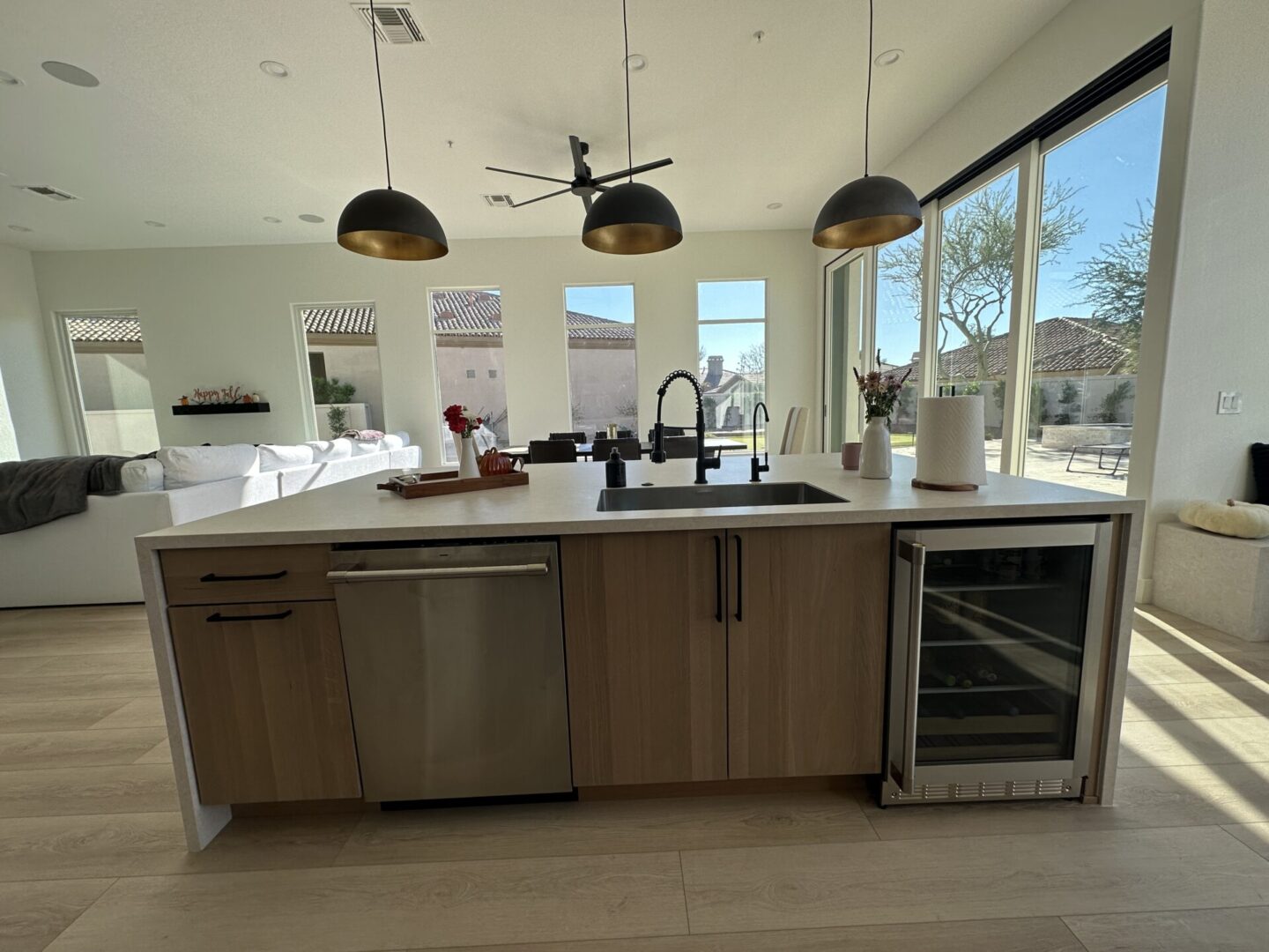 Modern kitchen island with wood cabinetry, stainless steel appliances, and black pendant lights overlooking living room and patio doors