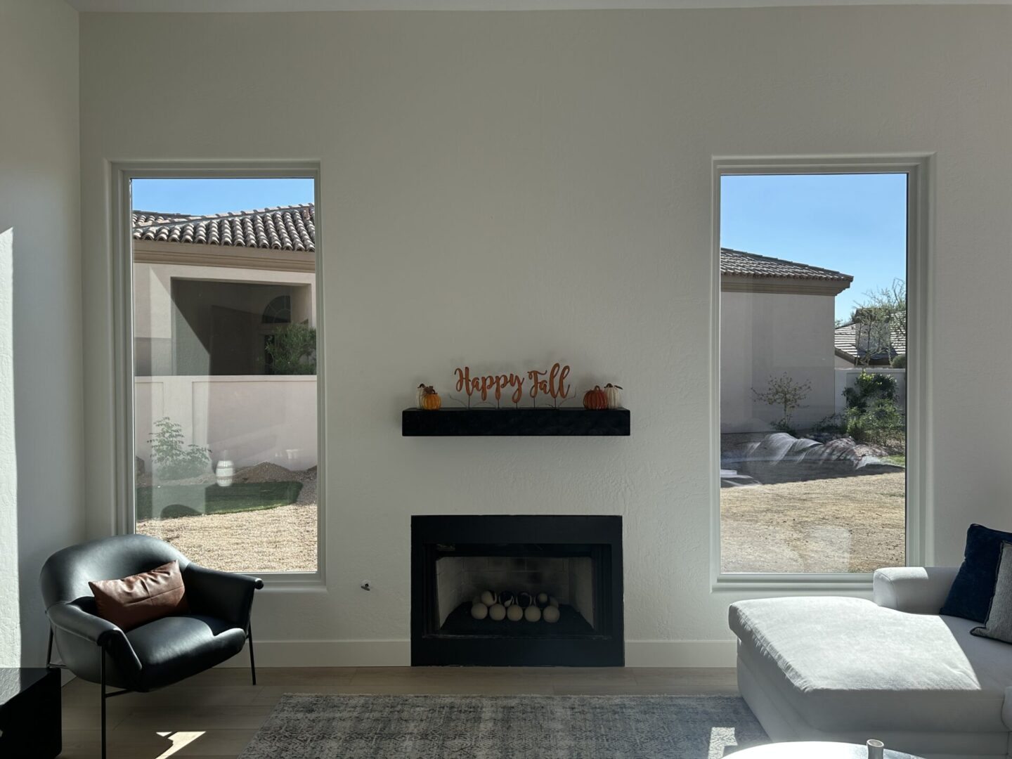 Modern living room with black fireplace, "happy fall" shelf decor, leather chair, large windows overlooking courtyard, and contemporary furnishings