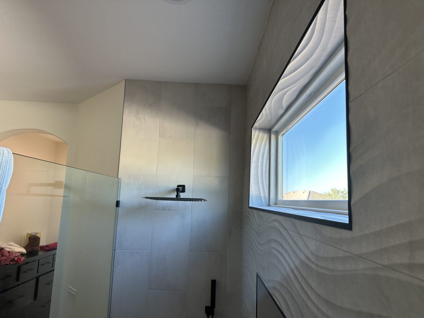 Modern bathroom with walk-in shower, glass enclosure, rainfall showerhead, and window with white curtains overlooking hillside landscape