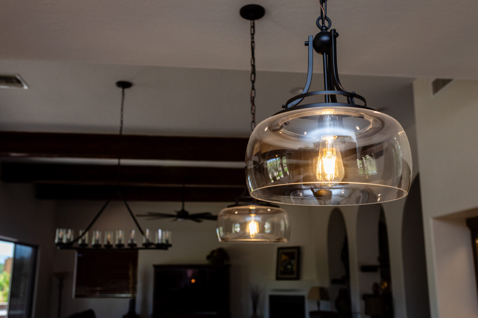 Modern kitchen with glowing pendant lights featuring clear glass shades and Edison-style filament bulbs hanging from black metal fixtures against white ceiling