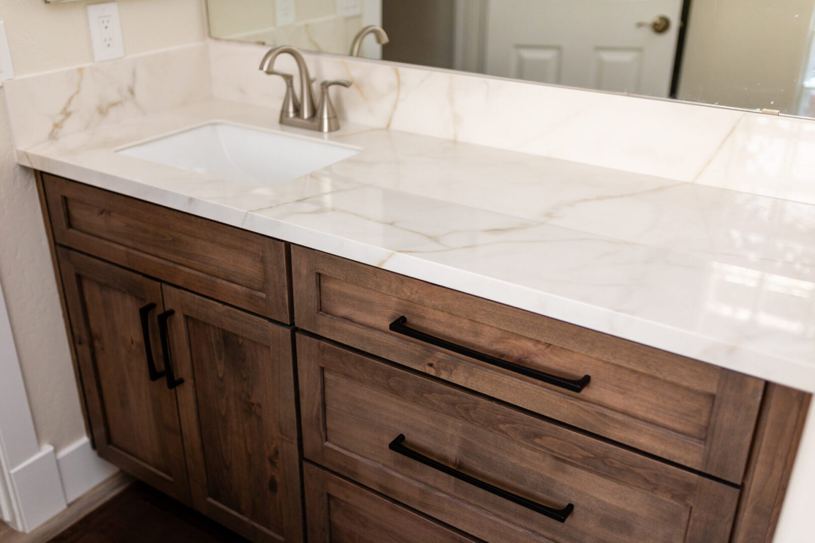 Modern bathroom vanity with dark wood cabinetry and white marble countertop featuring dual sink setup with brushed nickel faucet