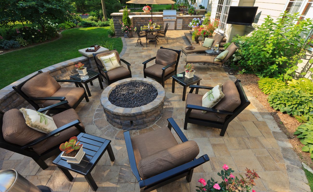 Luxurious backyard patio with stone fire pit, lounge chairs, dining area, outdoor kitchen, manicured lawn, and flowering gardens in Cincinnati home