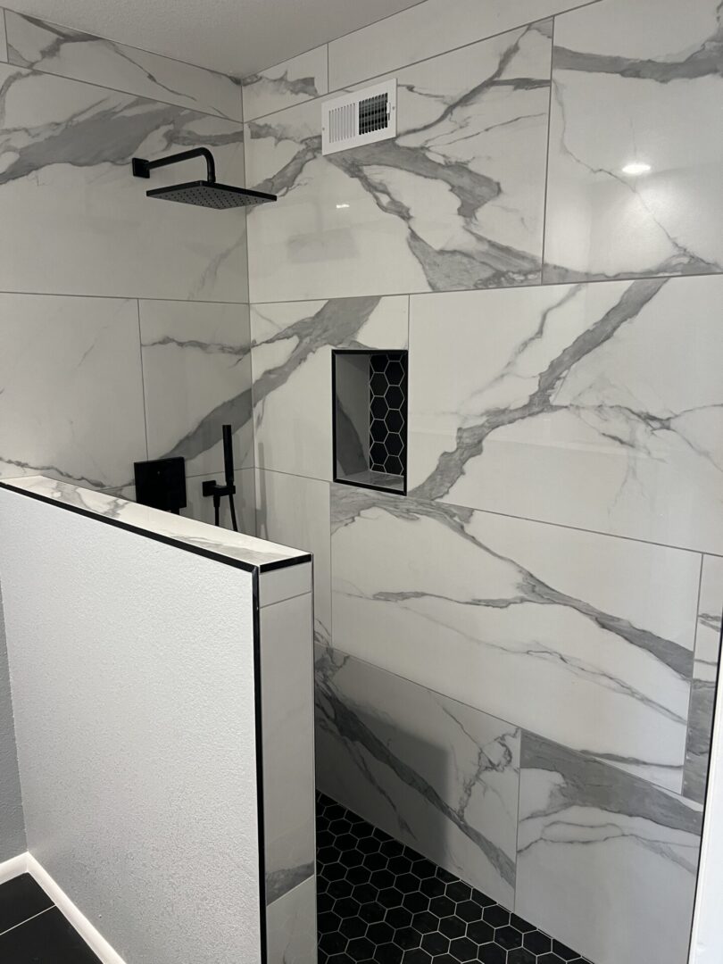 Modern walk-in shower with marble-effect tile walls, black fixtures, hexagonal floor tiles, and glass enclosure