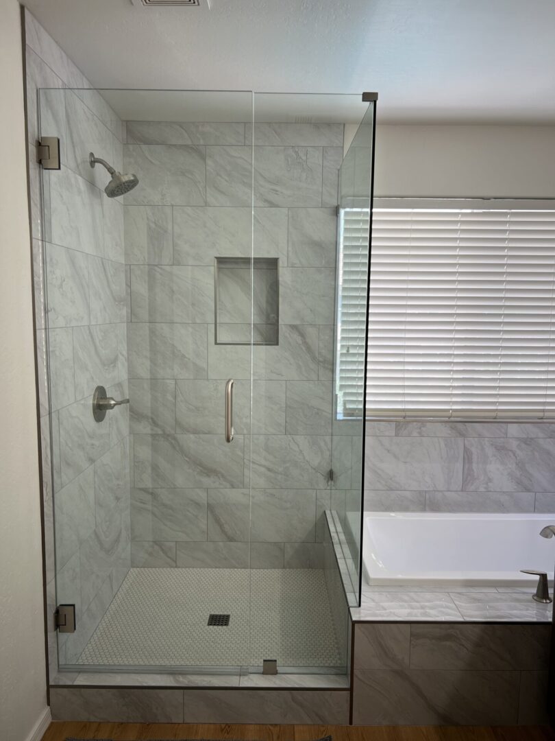 Modern bathroom with frameless glass shower enclosure featuring marble tile walls, rainfall showerhead, built-in niche, and white subway tile flooring with drain