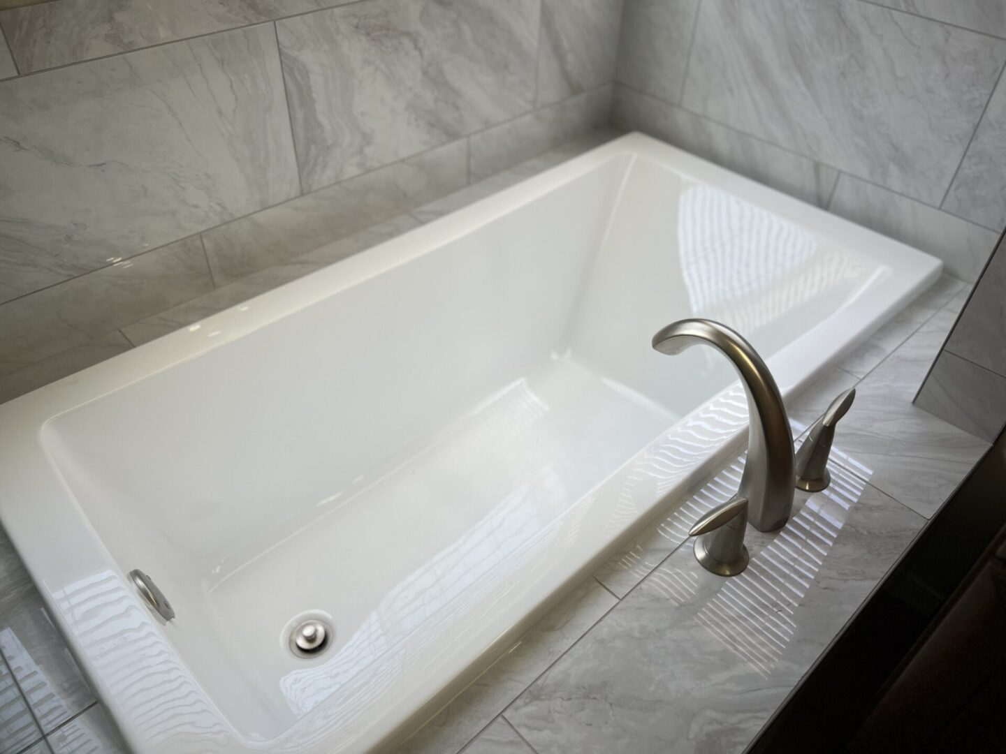 White bathtub with two-handle faucet and anti-slip mat in modern bathroom with gray tile walls