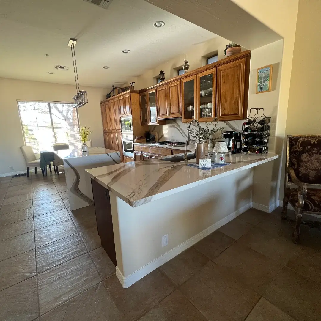 Modern kitchen with marble-topped island, wooden cabinetry, stainless steel appliances, and open floor plan connecting to dining area with natural light from large windows