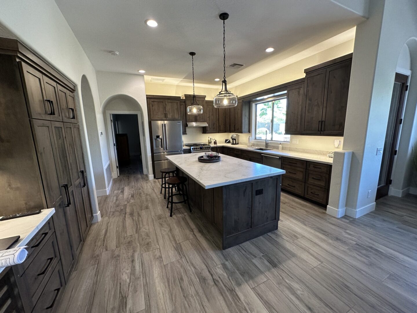 Modern kitchen with dark wood cabinetry, marble island countertop, stainless steel appliances, pendant lighting, and wood-look flooring