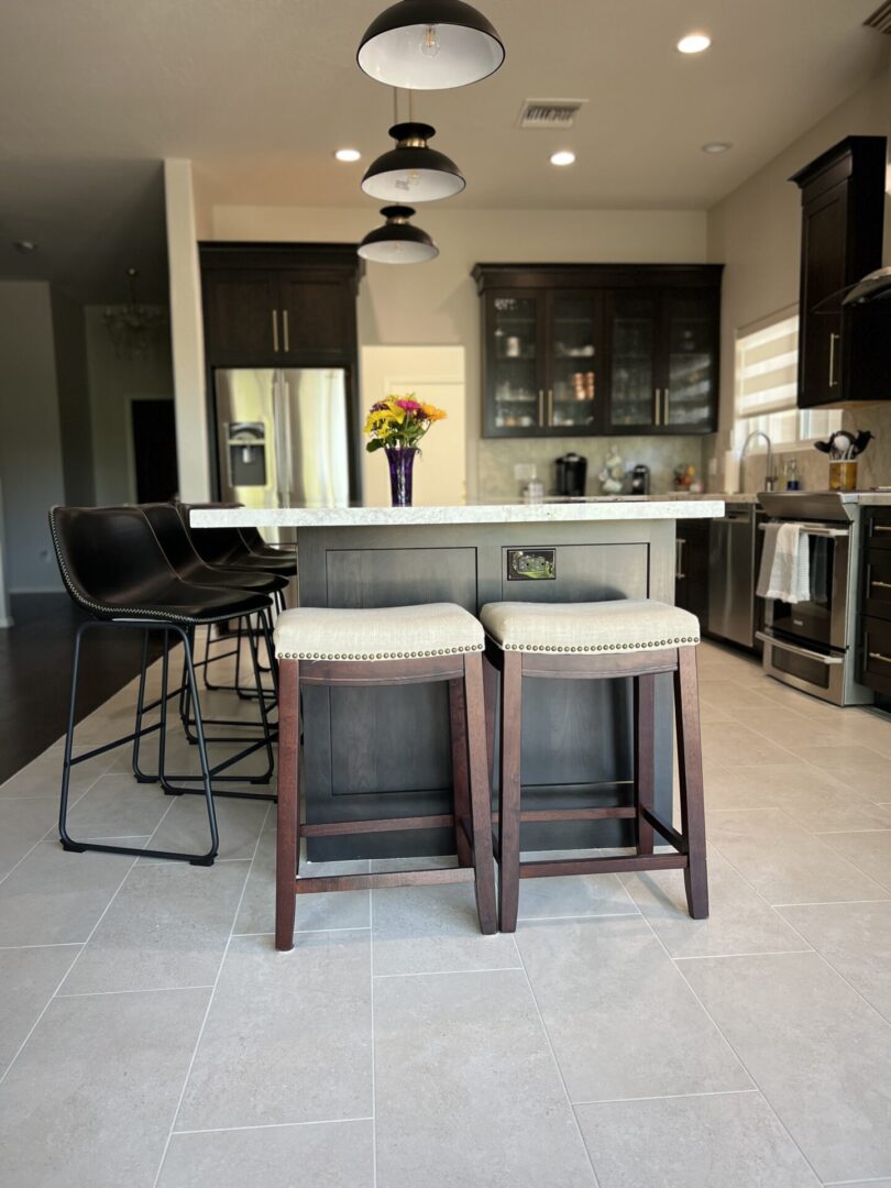 Modern kitchen with dark cabinetry, stainless steel appliances, white quartz island countertop, pendant lighting, and upholstered bar stools