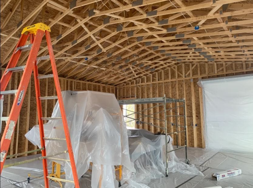 Interior construction site with wooden framing, red ladder, plastic-draped equipment, and metal scaffolding during renovation