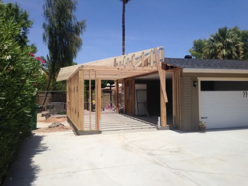Modern home addition with wood pergola structure, concrete driveway, and attached garage under clear blue sky with palm trees