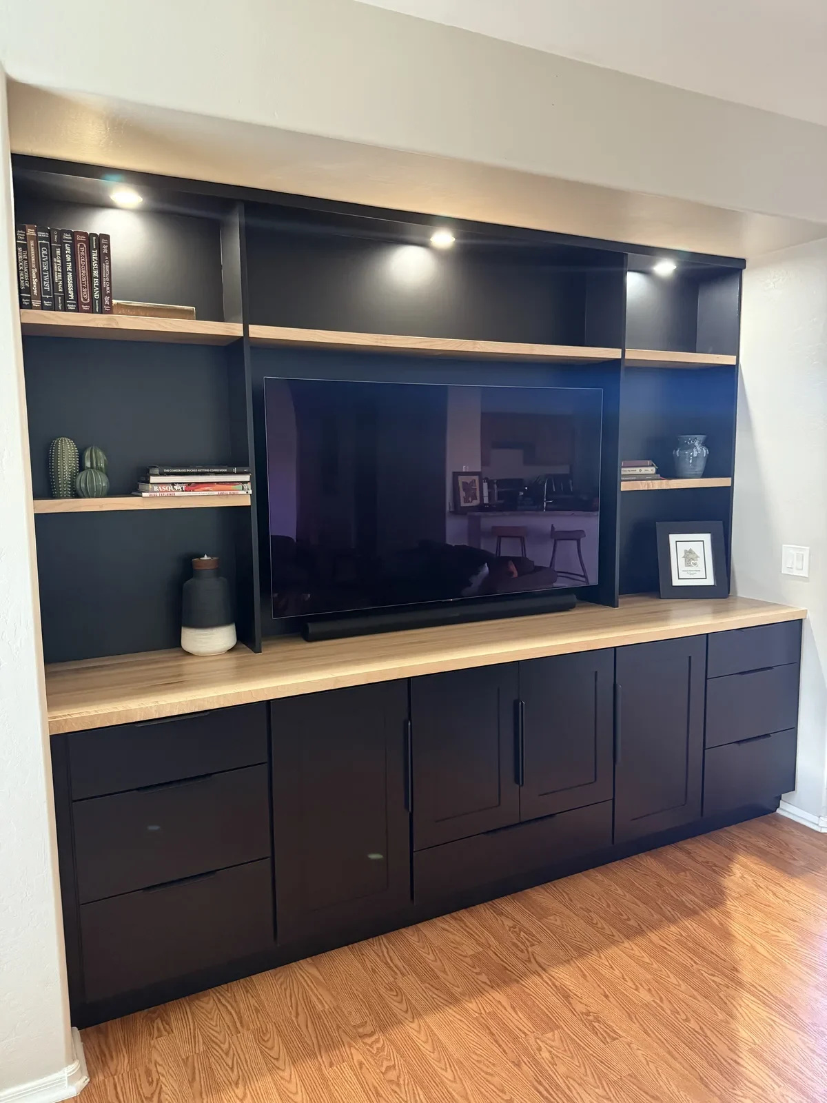 Modern dark blue built-in entertainment center with wood shelving, wall-mounted TV, and storage cabinets in contemporary home interior