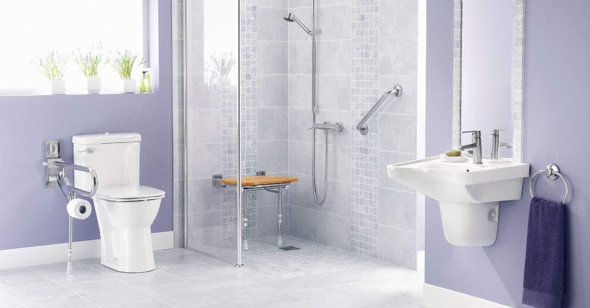 Modern accessible bathroom with lavender walls featuring a walk-in shower, toilet with grab bars, pedestal sink, and safety accessories