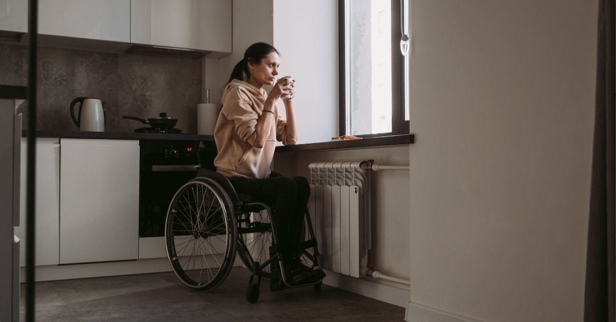 Woman in wheelchair drinking coffee in an accessible kitchen with modern appliances and large windows